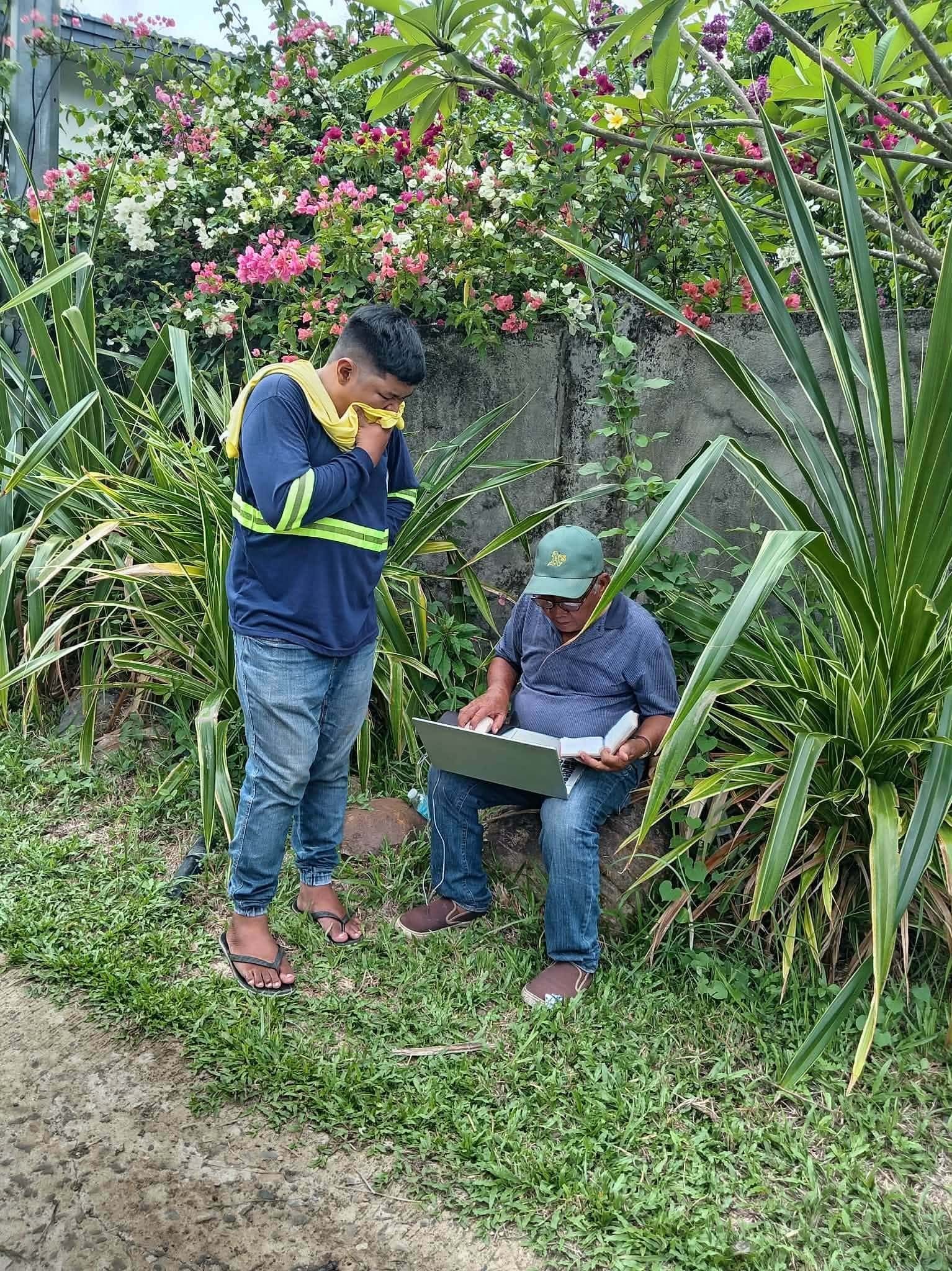 Two Leonor Surveying Services crew members reviewing survey records on a laptop outdoors in Murcia, Negros Occidental