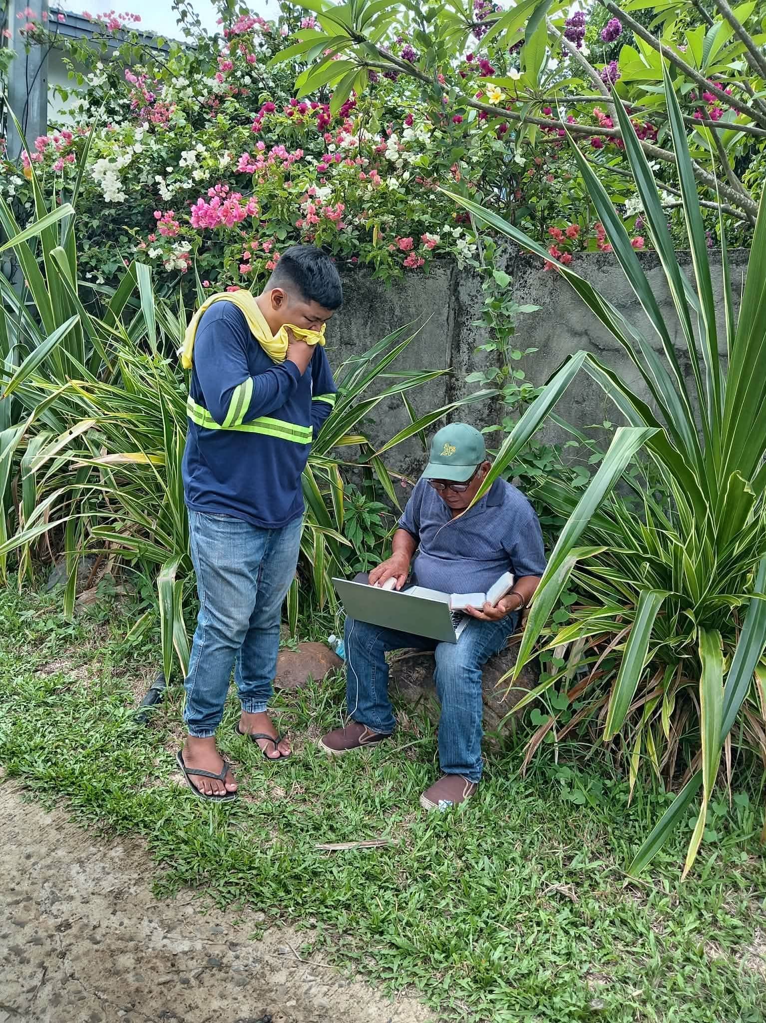 Two Leonor Surveying Services crew members reviewing land records on a laptop outdoors in Murcia, Negros Occidental