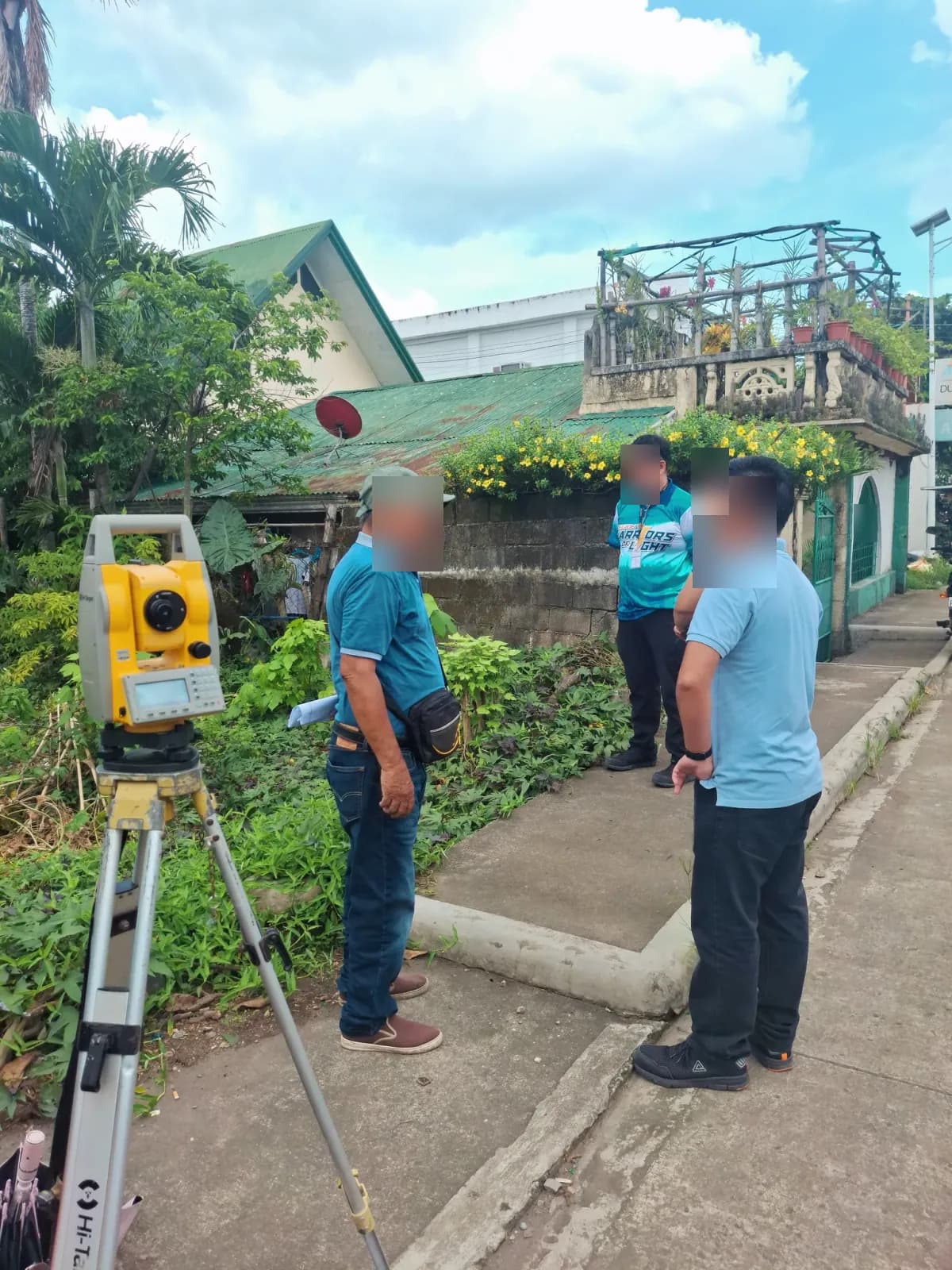 People discussing the roadside work beside a total station and a densely vegetated lot