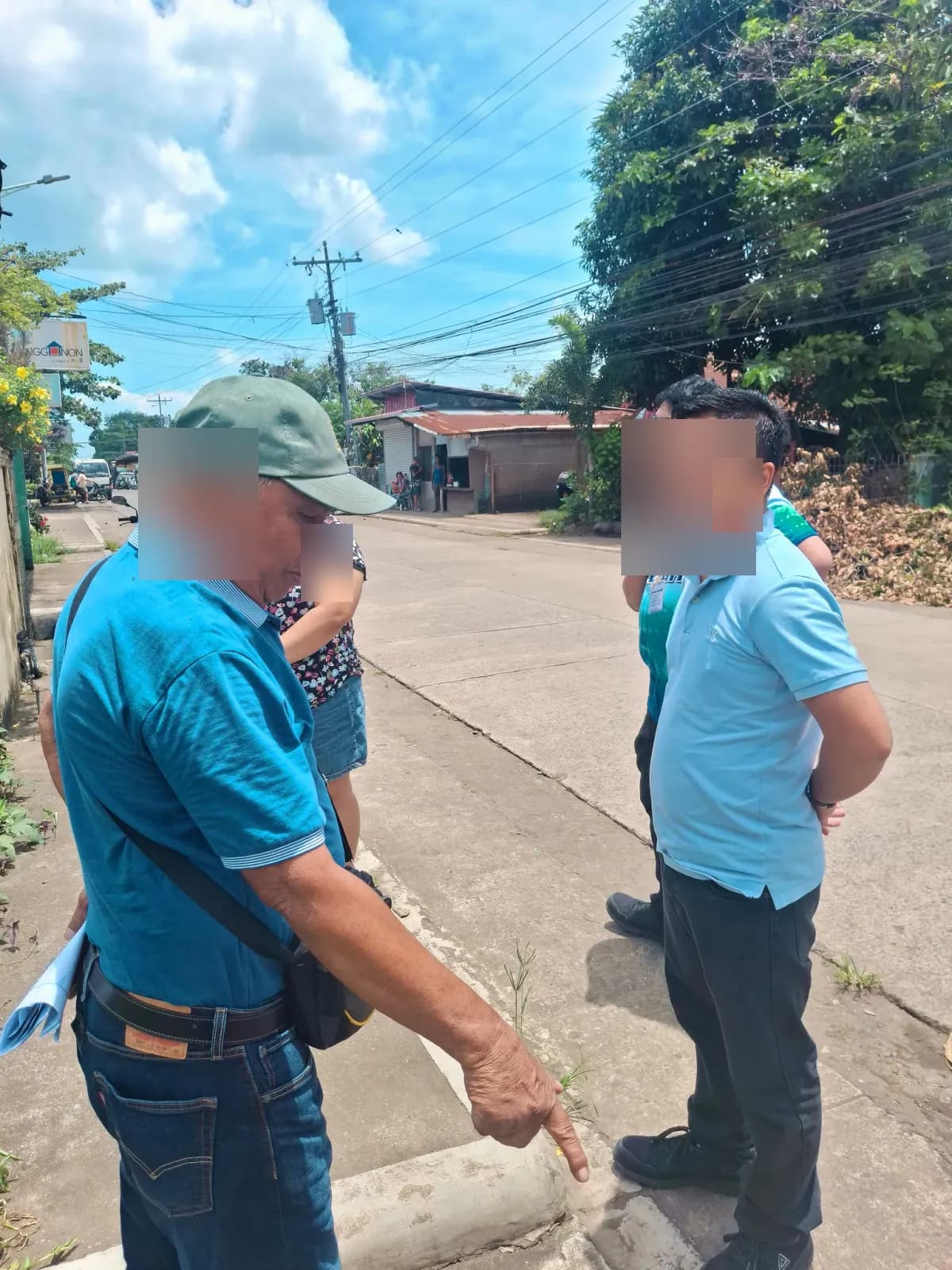 Roadside discussion with one person pointing toward the curb beside the vegetated lot