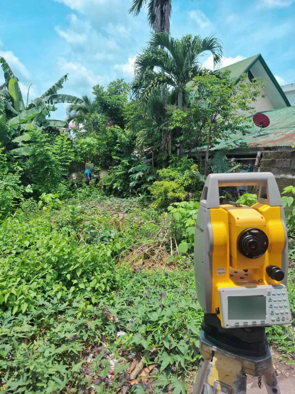 Close view of a total station aimed toward crew members among the vegetation