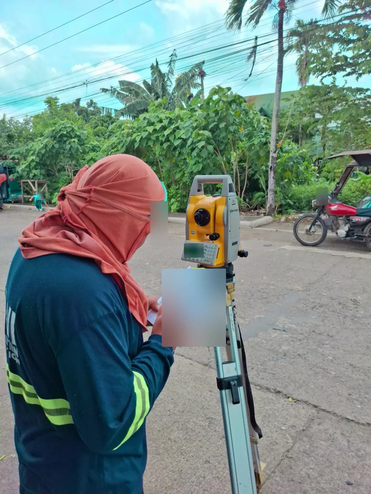 Survey operator recording field notes beside a total station at the edge of a neighborhood street