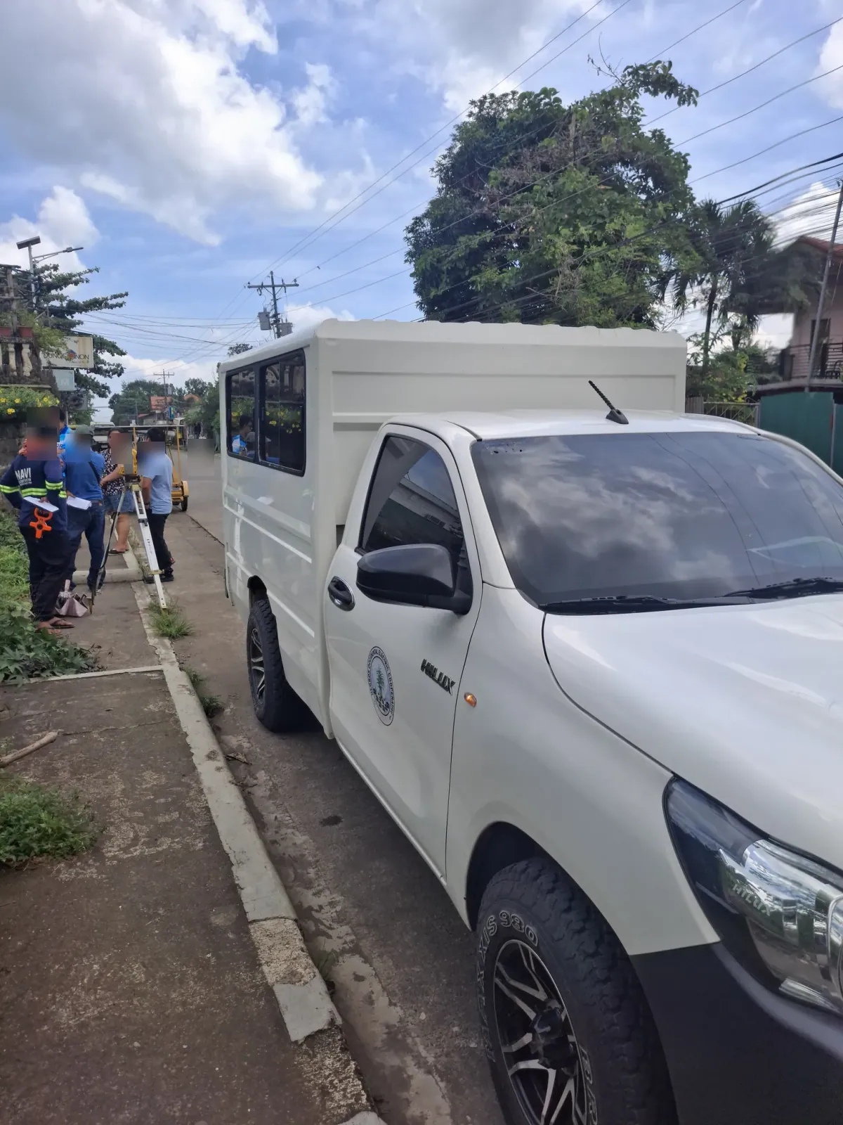 White utility vehicle parked beside the crew and total station on the sidewalk