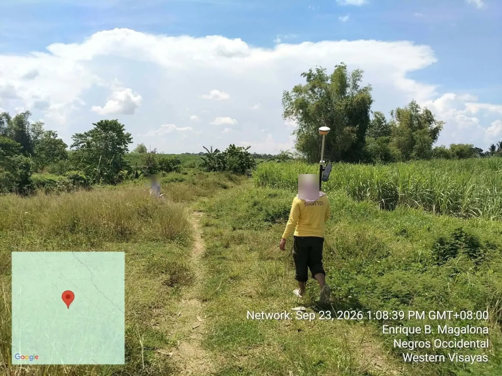 Survey crew carrying a GNSS pole along a grassy path between cultivated fields in E. B. Magalona