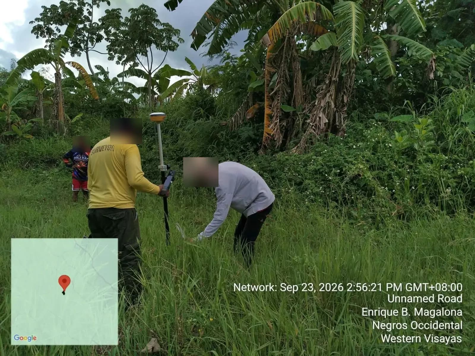 GNSS pole holder beside a crew member bending toward the ground in tall grass