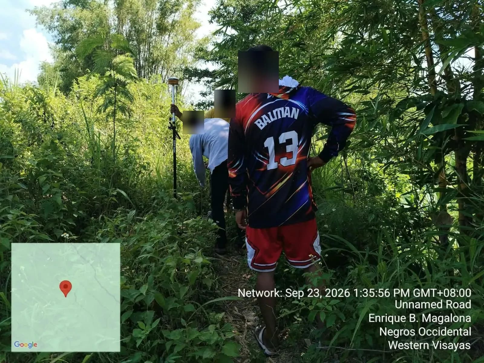 Field crew gathered around a GNSS pole on a shaded path bordered by bamboo